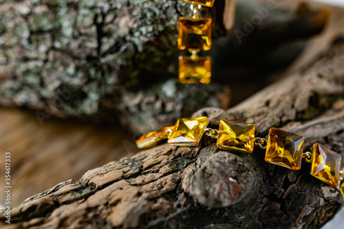 Beautiful and fashionable women's jewelry, elegant large yellow stones on a gold base, square shape, hanging on the bark and wooden natural snags