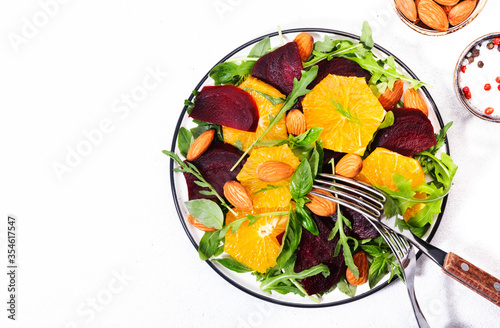 Beetroot Salad with Orange, arugula and almonds nut on white background. Vegan healthy summer food. Top view. Copy space