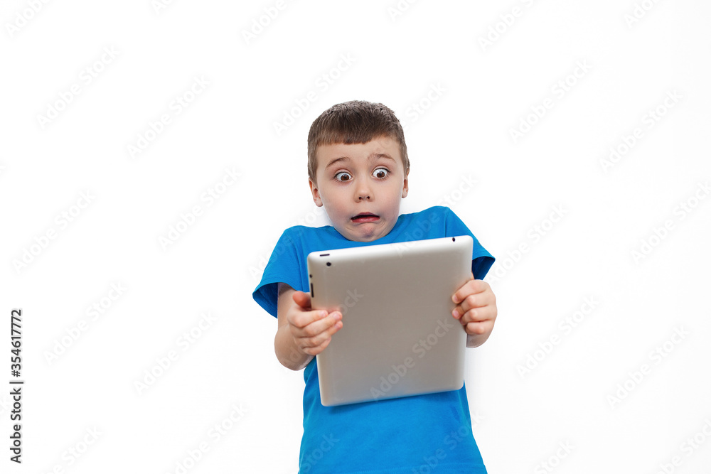 Surprised child in a blue t-shirt with a computer on a white background, isolated Surprised child in a blue t-shirt with a computer on a white background, isolated
