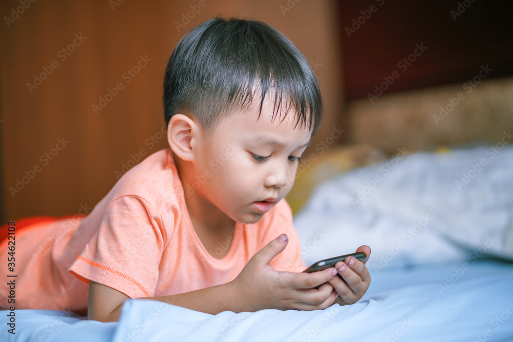little asian boy lying on the bed using and looking at smartphone 