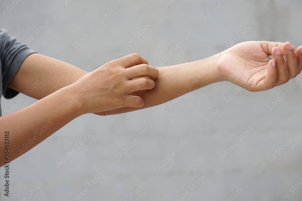Woman scratching arm from itching on light gray background. Cause of itchy skin include insect bites, dermatitis, food/drugs allergies or dry skin. Concept of health care skin.