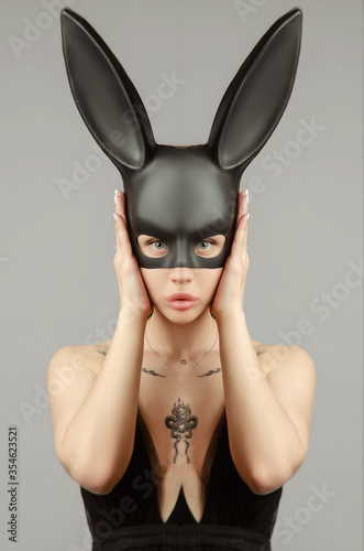 Beautiful blonde in a rabbit mask in a sexy evening dress on a white background with a metal chain