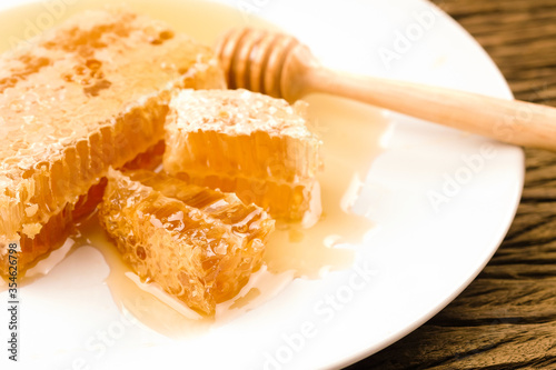 Honey with sweet honeycomb and dipper on a white plate
