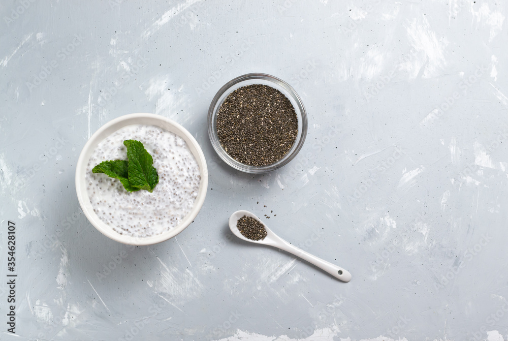 Chia pudding with mint leaves in a white bowl and a glass bowl with grains on a gray background. Top view. A healthy breakfast consists of yogurt and chia beans. Copy space. Chia pudding with mint leaves in a white bowl and a glass bowl with grains on a gray background. Top view. A healthy breakfast consists of yogurt and chia beans. Copy space.