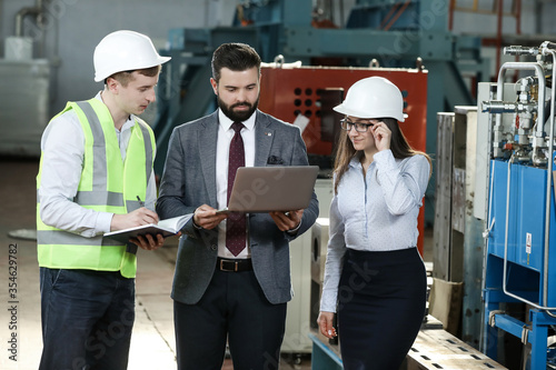Portrait of a solid businessman with his secretary and factory engineer holding laptop, talking about factory financial report in a airplane manufactory.