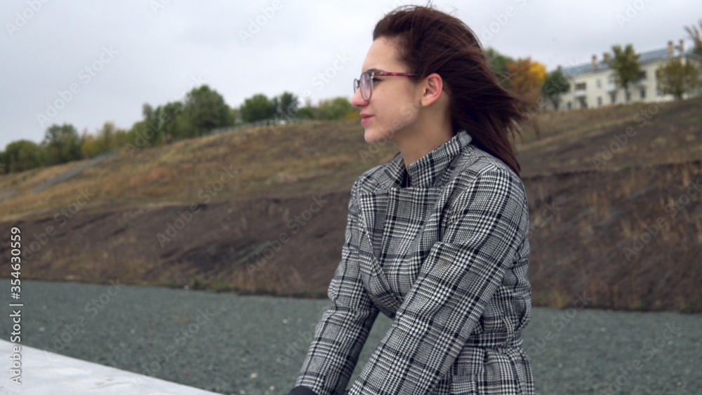 Young woman sits on a concrete fence in the wind