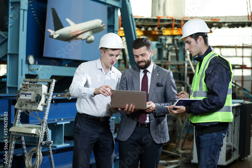 Portrait of a 3 men in a airplane manufactory. Two company managers and one factory worker deciding future plans. Business solution. 