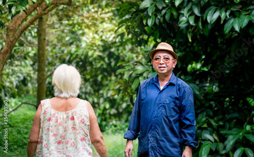 Happy Thai gardener man and grandmother walking at his organic garden. Sufficiency economy.Proud with success gardener man with organic orchards such as durian, rambutan, longkong, pepper, mangosteen.