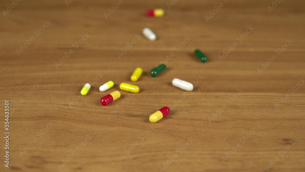 Multi-colored pills and capsules fall on the table