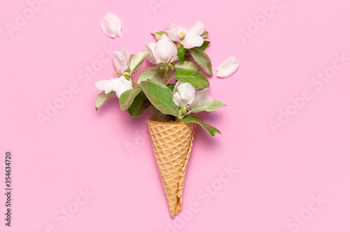 Creative spring minimal concept. Waffle cone with bouquet of spring blooming branches of white flowers and green leaves on pink background. Flat lay top view copy space. Spring nature background