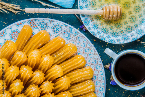 Top view of syrupy dessert tulumba arranged in plate. Turkish syrupy pastry arranged in plate on table with cup with coffee and honey. photo