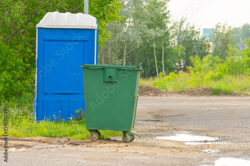 Green trash can and portable toilet on a background of greenery