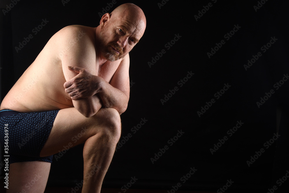 dark portrait of a shirtless man on black background leaning on his leg