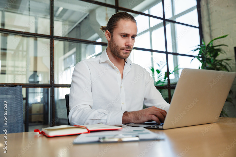 Photo of handsome serious man working with laptop while sitting Photo of handsome serious man working with laptop while sitting