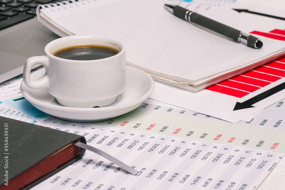 Office Desk of a company employee with a Cup of coffee, Notepad, computer and financial documents. Work at home or in the office. Office Desk of a company employee with a Cup of coffee, Notepad, computer and financial documents. Work at home or in the office.