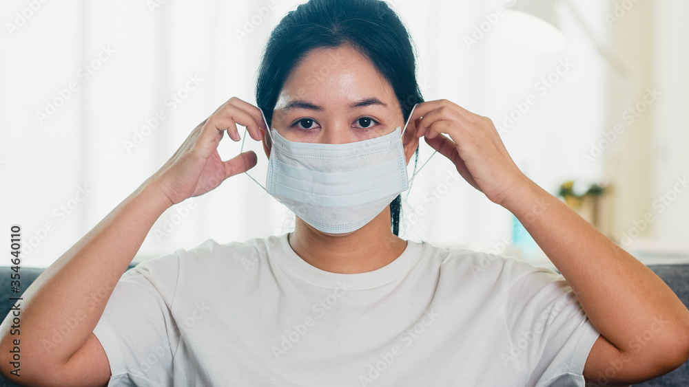 Depressed Asian business woman wearing protective mask sitting on sofa in living room at house when social distancing stay at home and self quarantine time, pandemic in china, coronavirus concept.