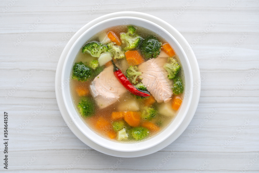Fresh salmon fish soup with carrots, potatoes, red peppers, green broccoli and onions in a white plate, close up. Tasty dinner consists of a fish soup with salmon Fresh salmon fish soup with carrots, potatoes, red peppers, green broccoli and onions in a white plate, close up. Tasty dinner consists of a fish soup with salmon