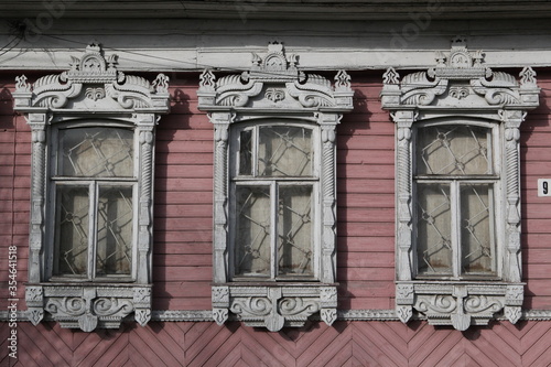 Richly decorated ornamental carved windows, frames on vintage pink wooden rural house in Lukh village, Ivanovo region, Russia. Russian traditional national style in wooden architecture. Countryside photo