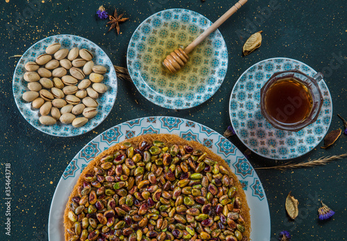 High angle view of kadayif with pistachios and honey. Oriental dessert of kadaif noodles on table with pistachios, plate with honey and cup of tea. photo
