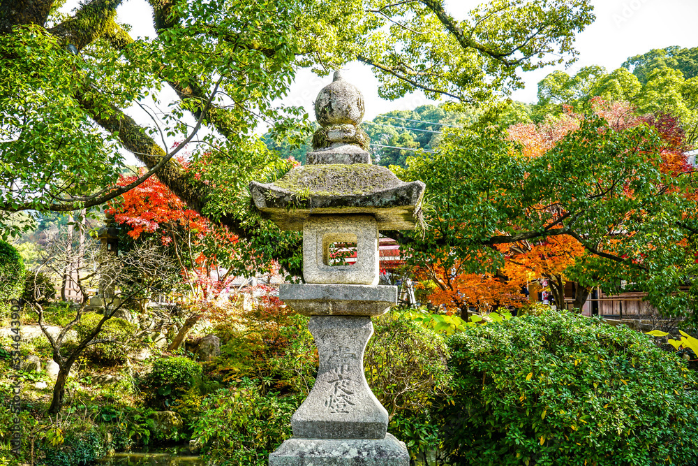 A peaceful background of autumn Japanese garden and a traditional granite stone lamp post in the middle A peaceful background of autumn Japanese garden and a traditional granite stone lamp post in the middle