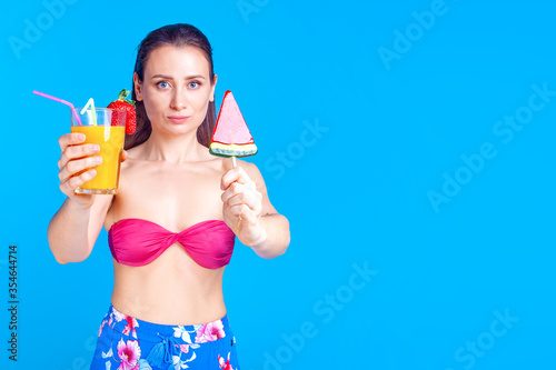 woman in a swimsuit and a cocktail in hands on a blue background in the studio