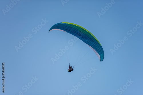 Paragliders with multi-colored parachutes fly high in the clear blue sky over steep cliffs. Parachuting, adrenalitis, love of height, risk, freedom of action. Desire to be able to fly