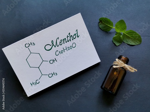 Structural chemical formula of menthol molecule with fresh mint leaf and a glass cosmetic bottle. Peppermint essential oil, concept of aromatherapy, cosmetic and health. photo