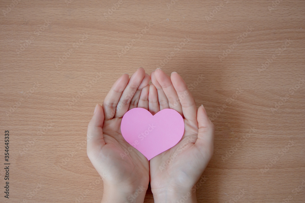 Hand holding pink heart on wood table background, healthcare, organ donation, love, hope and giving concept.