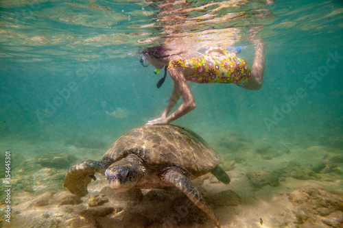 A girl swims with a large turtle in the sea ocean near a coral reef in Sri Lanka.