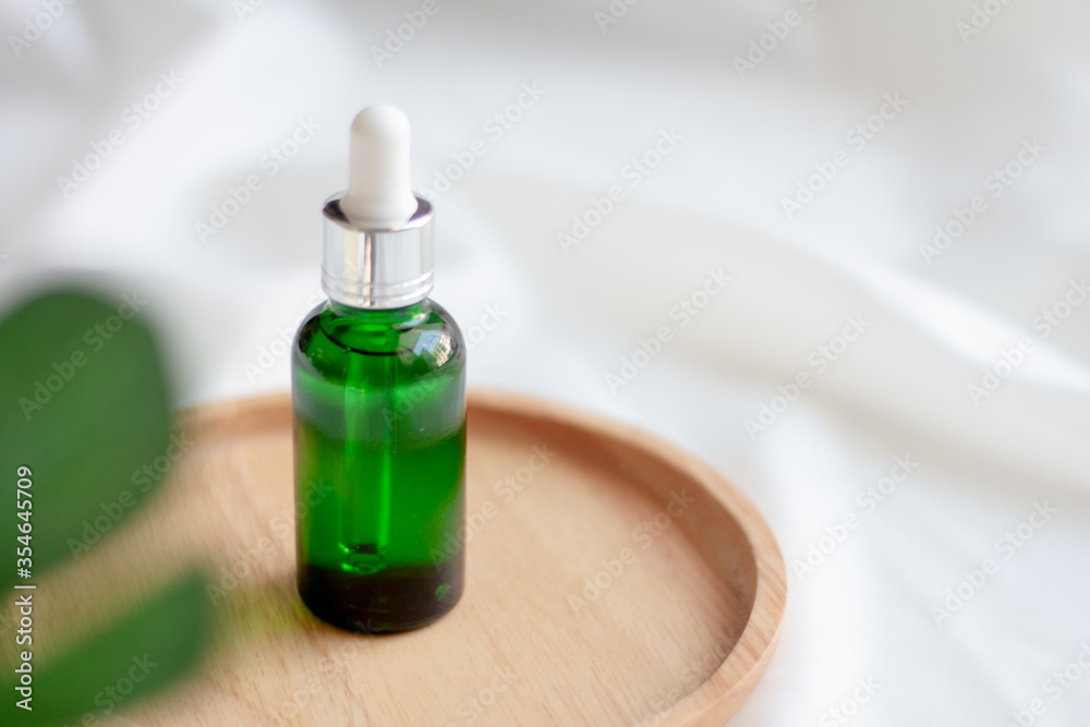 Green dropper bottle serum on wood plate. Natural facial essential oil or serum packaging on white fabric background. Beauty product branding mock-up. Cosmetic skincare concept. Cruelty-free. Green dropper bottle serum on wood plate. Natural facial essential oil or serum packaging on white fabric background. Beauty product branding mock-up. Cosmetic skincare concept. Cruelty-free.