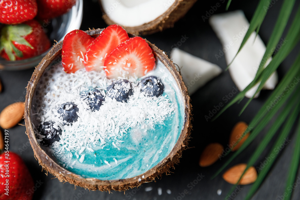 Blue smoothie bowl in coconut shell with berry chia seeds pudding and granola. Blue smoothie bowl in coconut shell with berry chia seeds pudding and granola.