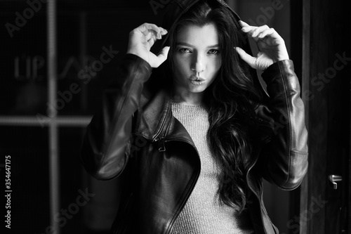 Gorgeous brunette girl with curly hair. Black and white photo. The lady is wearing a leather jacket. Her look is aggressive and seductive.
