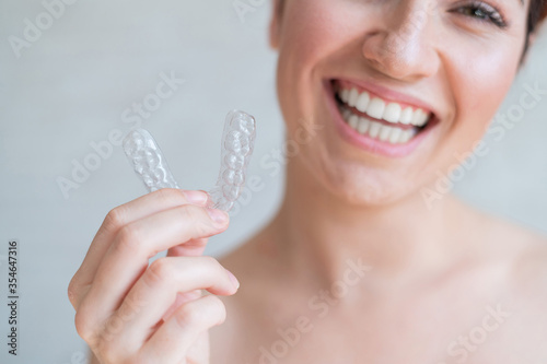 Close-up of orthodontic silicone transparent teeth aligner in female hands. A woman with a perfect charm smile holds a removable night retainer. Bracket for teeth whitening. Cropped photo.