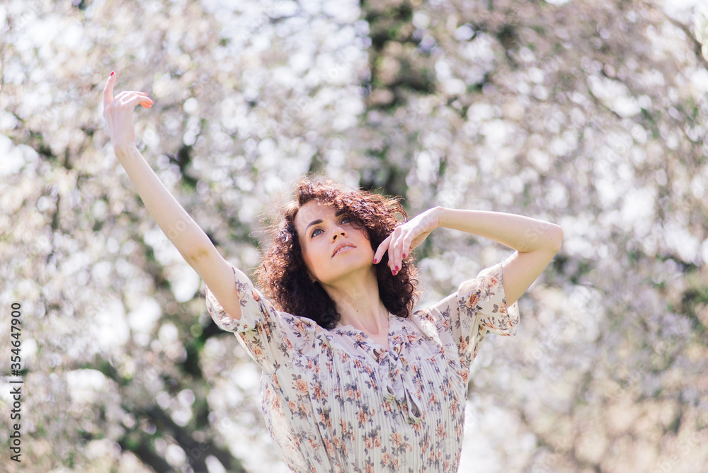 Young attractive woman with curly long hair posing in spring blooming garden, apple trees