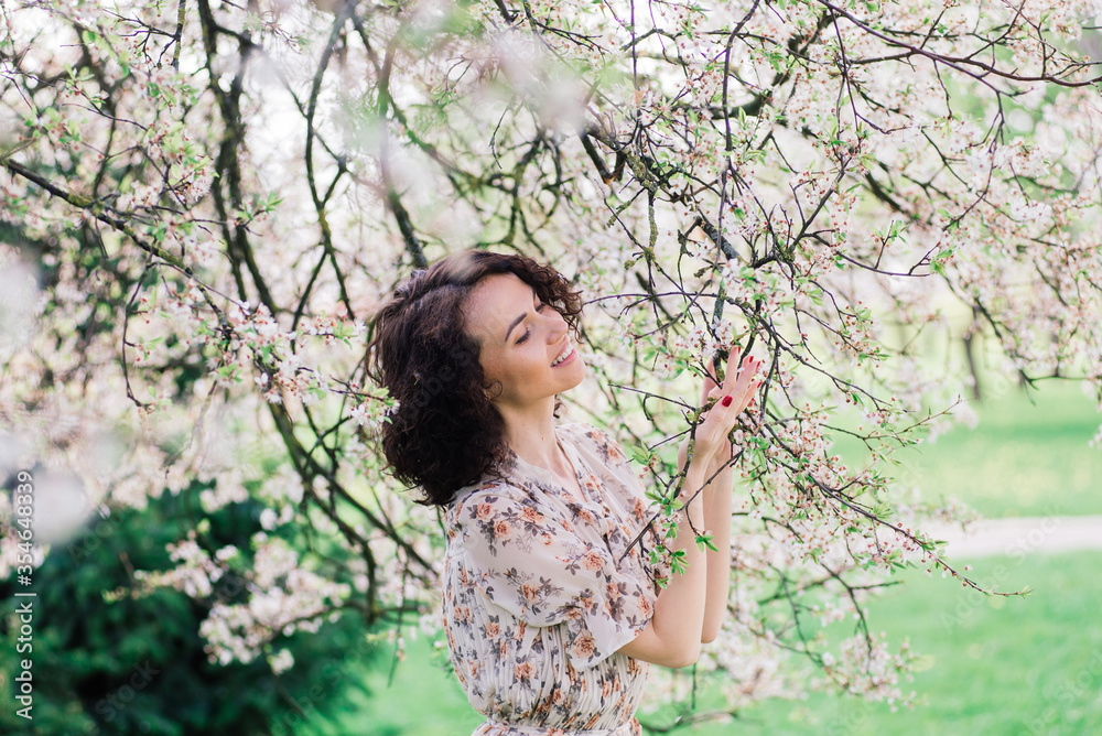 Young attractive woman with curly long hair posing in spring blooming garden, apple trees Young attractive woman with curly long hair posing in spring blooming garden, apple trees