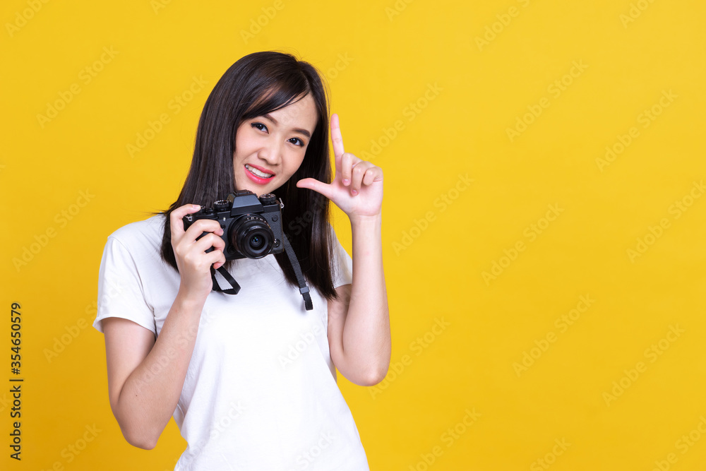 Fototapeta premium Portrait photo of Asian smiling pretty girl in white shirt taking photo on camera isolated over orrange background