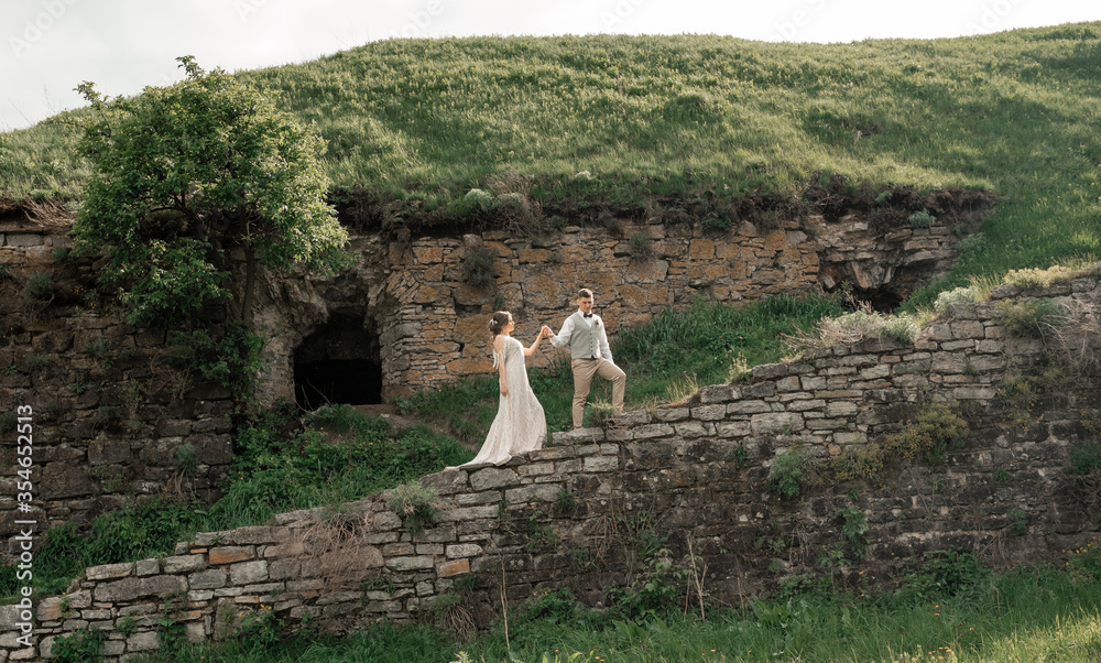 Naklejka premium Happy loving couple. Traveling, holidays, vacation, love story and friendship concept - smiling couple holding hands in green landscape