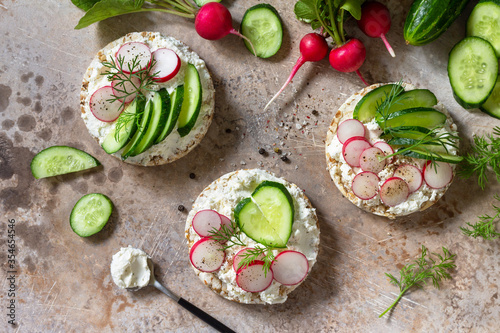 Crispbread sandwiches with ricotta, radish and fresh cucumber on a light kitchen stone or slate countertop. Top view flat lay background.