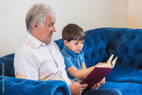 Grandfather and grandson read a book while sitting on the sofa while relaxing