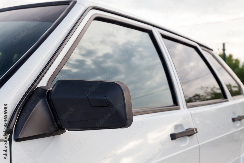 Close-up of a plastic black side mirror and handles on the front of the auto mirror housing of a Russian VAZ 2114 car with white metal doors.