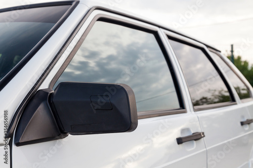 Close-up of a plastic black side mirror and handles on the front of the auto mirror housing of a Russian VAZ 2114 car with white metal doors.