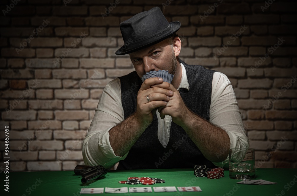 Poker player with cards and playing chips a the poker table - poker in a dark back room with a brick wall Poker player with cards and playing chips a the poker table - poker in a dark back room with a brick wall