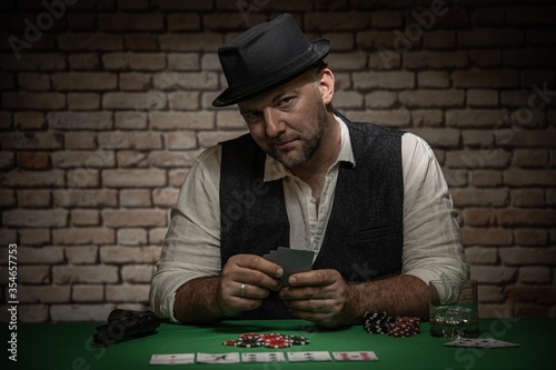 Poker player with cards and playing chips a the poker table - poker in a dark back room with a brick wall