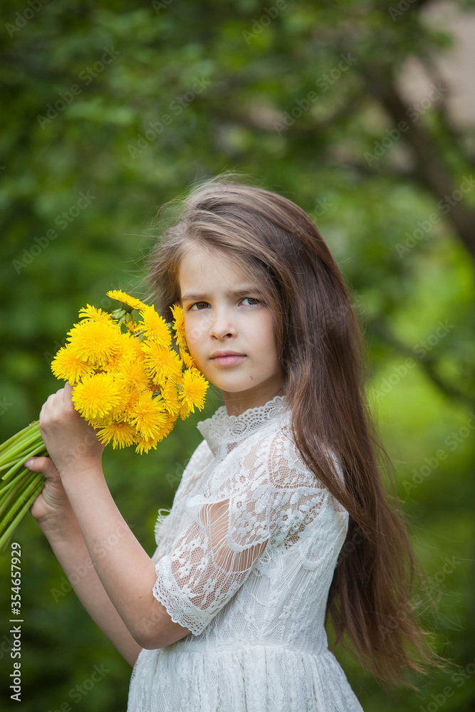 A fashionable girl in a beautiful white dress poses with yellow dandelion flowers in green foliage A fashionable girl in a beautiful white dress poses with yellow dandelion flowers in green foliage