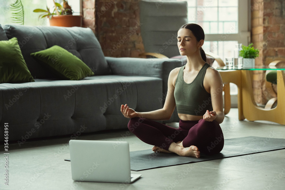 Balance. Sporty beautiful young woman taking professional yoga lessons online and practice at home. Concept of healthy lifestyle, wellness, wellbeing, looking for new hobby. Flexible and motivated. Balance. Sporty beautiful young woman taking professional yoga lessons online and practice at home. Concept of healthy lifestyle, wellness, wellbeing, looking for new hobby. Flexible and motivated.