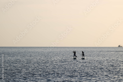 Couple of man and woman paddle on the surf board happily together under the sunset sky