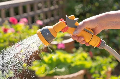 Hand holding a watering hose spray gun watering plants in a garden. UK photo
