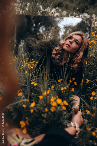 Photo session of a stylish girl outdoors with a mirror. Young model on a background of yellow flowers.