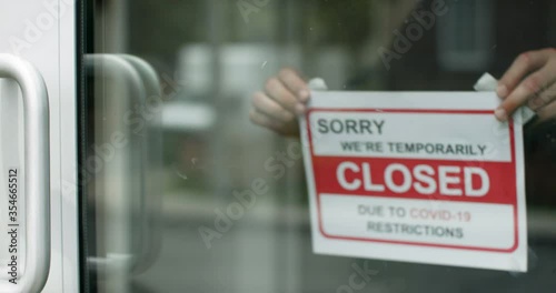 Closed for business due to covid. Small shop puts closed sign up on storefront. Business closes due to covid. A sign put up on shopfront. Shot in slow-motion in 4k. photo