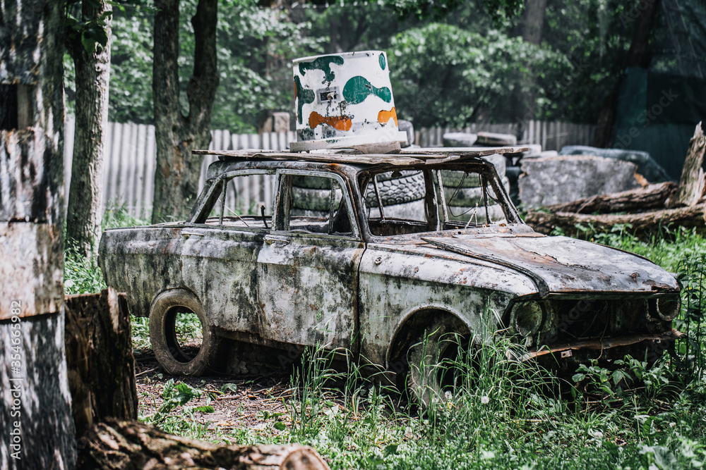 Paintball shooting range. Paintball territory in the forest. Old car in the foreground with multi-colored blots and smudges from shots from the paintball weapon. Old tires from a car and trees. 